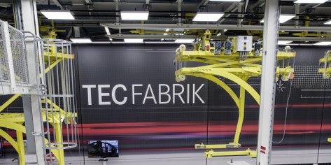 Ausschnitt aus der TEC Fabrik, Produktions-Roboter im Vordergrund, leere silberne KFZ-Karosserie, im Hintergrund an der Decke befestigte Fördereinheit 
